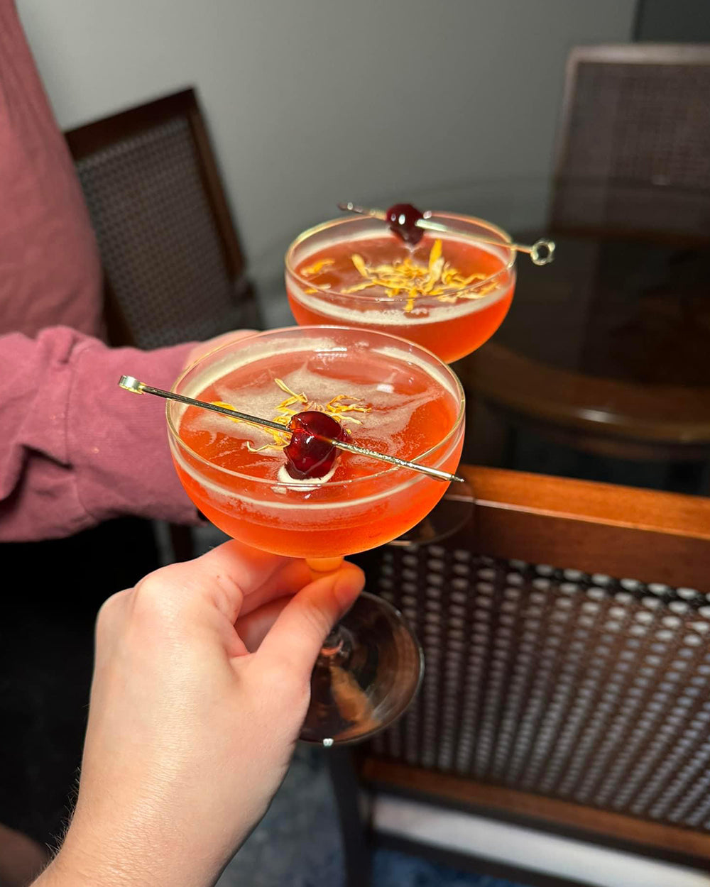 Two people cheersing orange non-alcoholic cocktails with glass table in background.