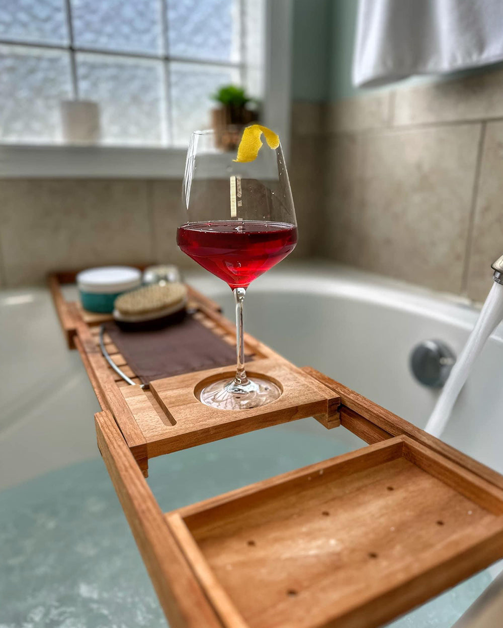 Glass of non-alcoholic win on tray in a bathtub.