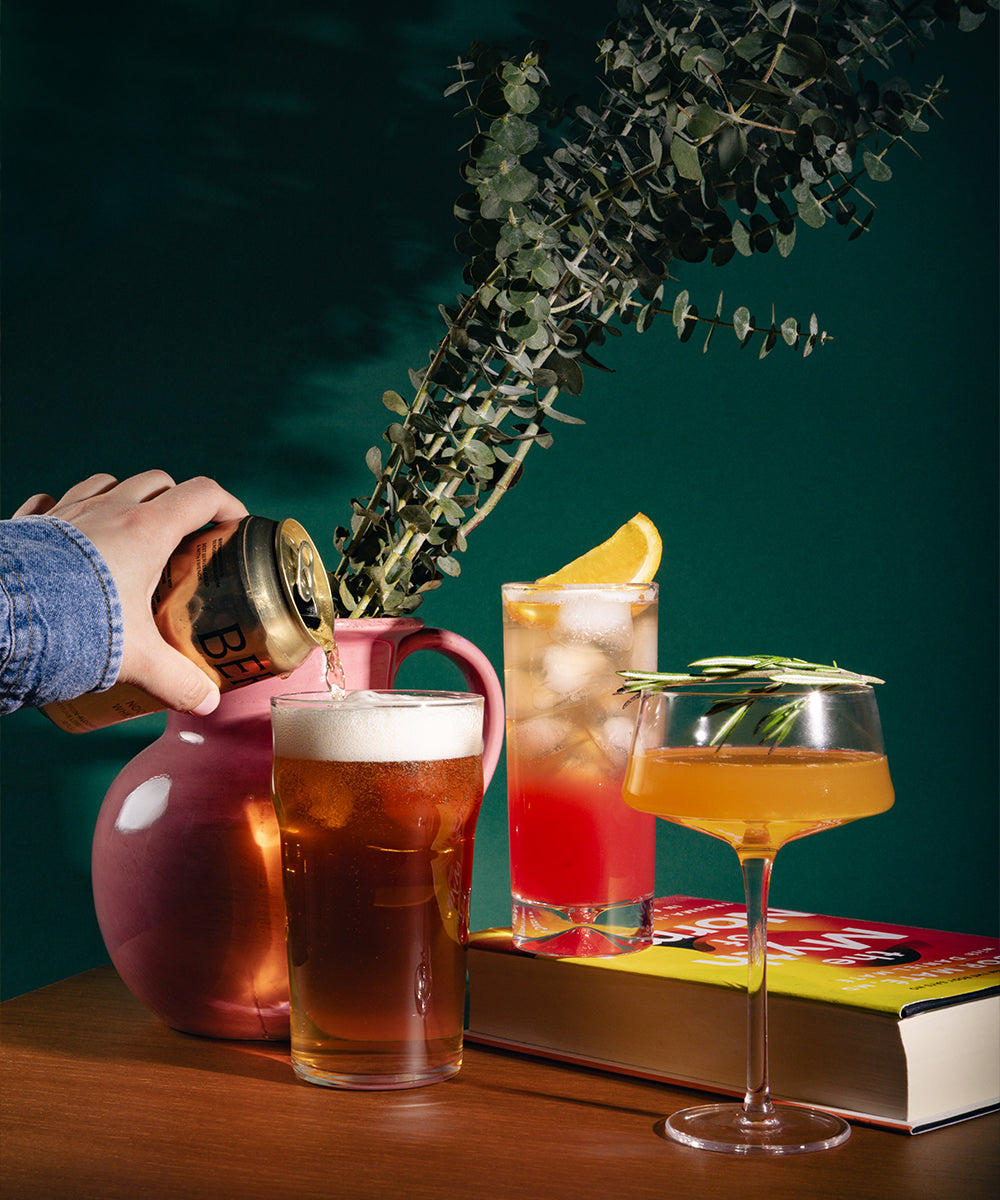 Gold Standard box non-alcoholic cocktails on wood surface beside vase and book.