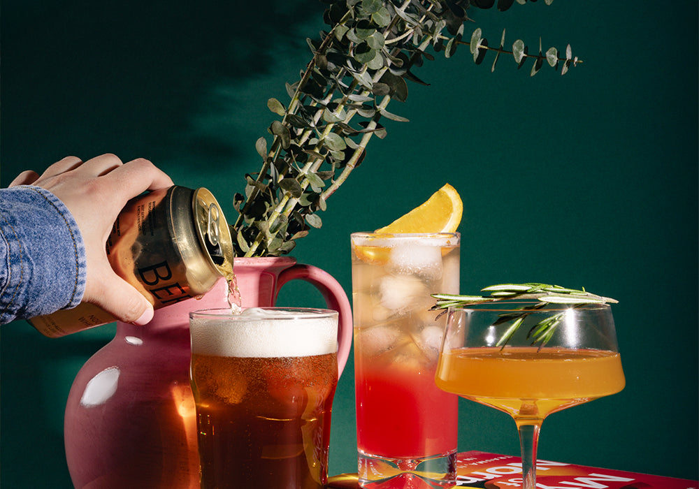 Gold Standard box non-alcoholic cocktails on wood surface beside vase and book.