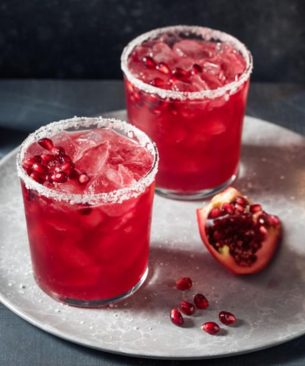 Two red cocktails with pomegranate seeds on a metallic tray