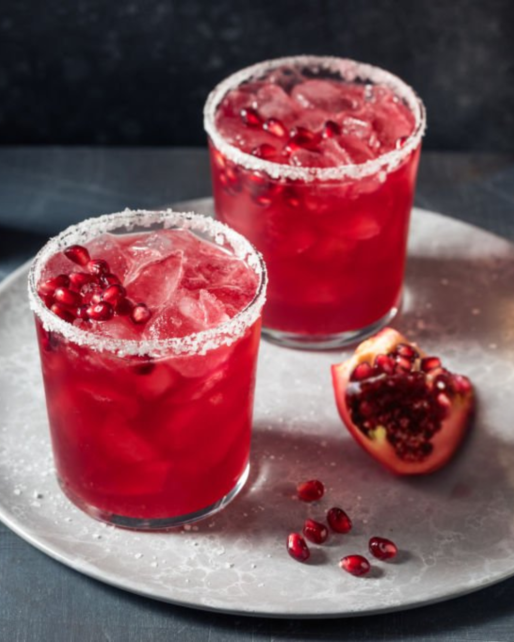 Two red cocktails with pomegranate seeds on a metallic tray