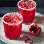 Two red cocktails with pomegranate seeds on a metallic tray