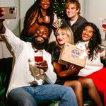 Group of friends taking a selfie together in a festive setting with a Christmas tree.