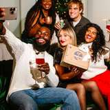 Group of friends taking a selfie together in a festive setting with a Christmas tree.