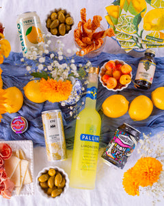 Various non-alcoholic cocktails and ingredients scattered on table with various fruits, flowers and blue cloth.