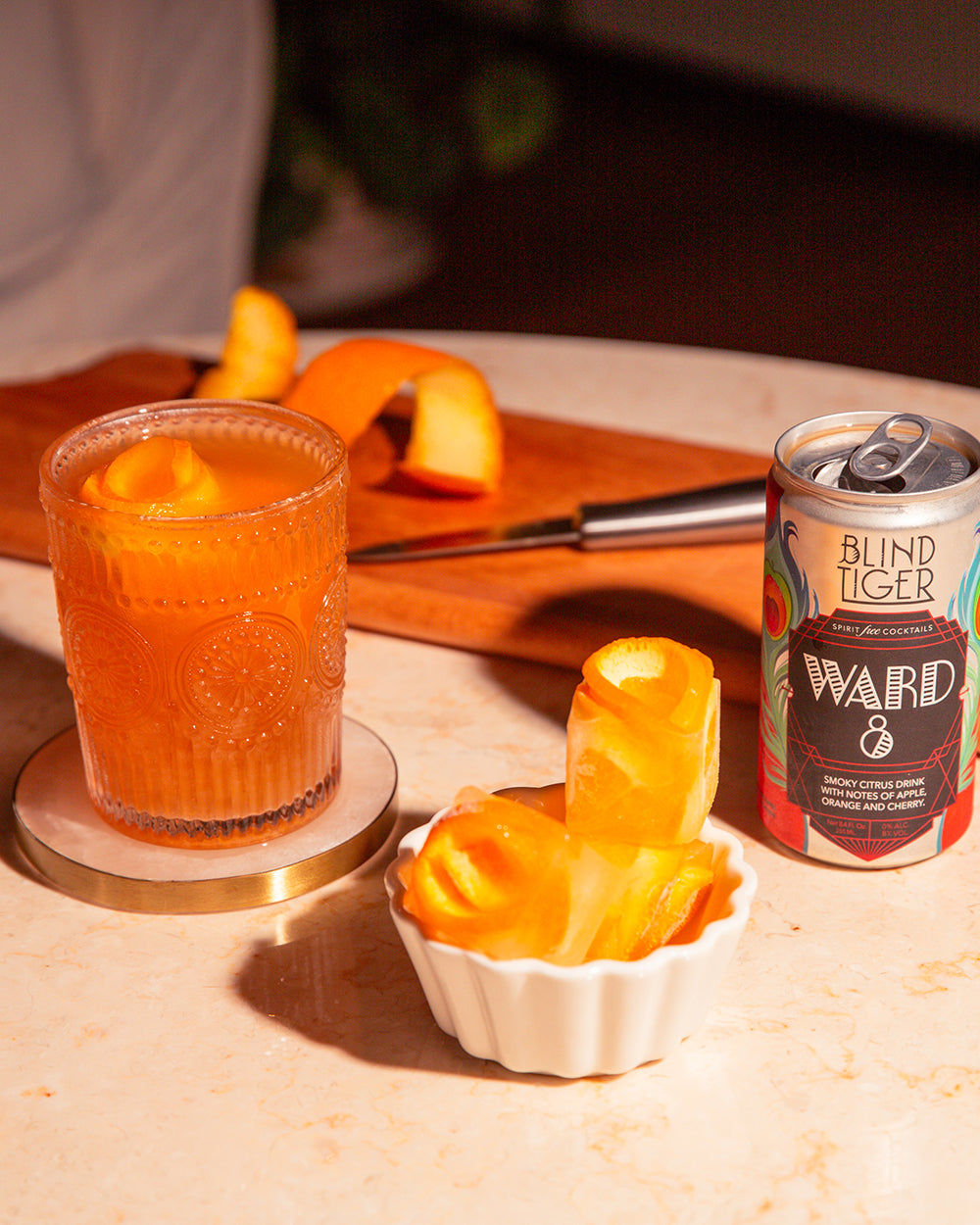 Linger zero-proof cocktail on marble table beside orange peels and Blind Tiger can.