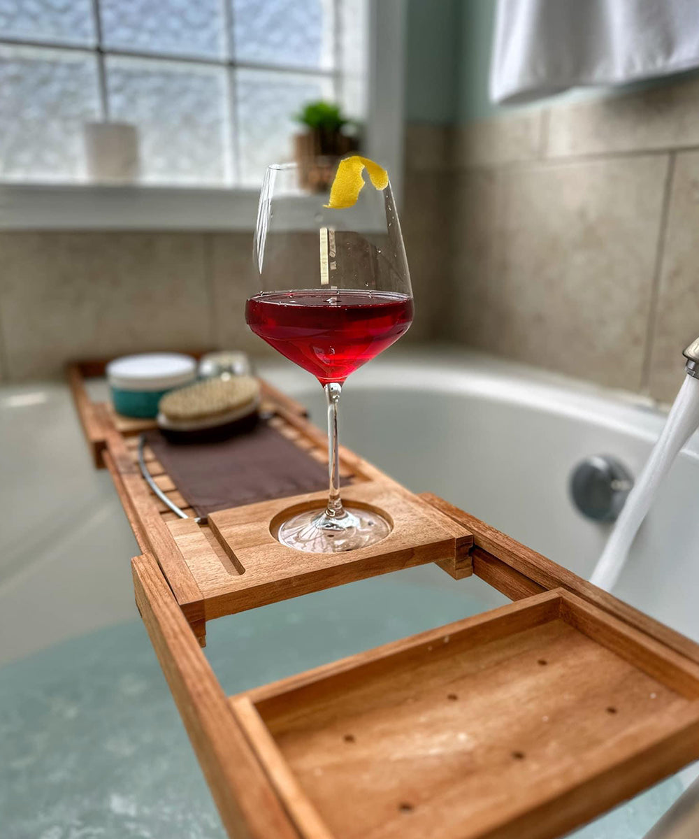 Glass of non-alcoholic win on tray in a bathtub.