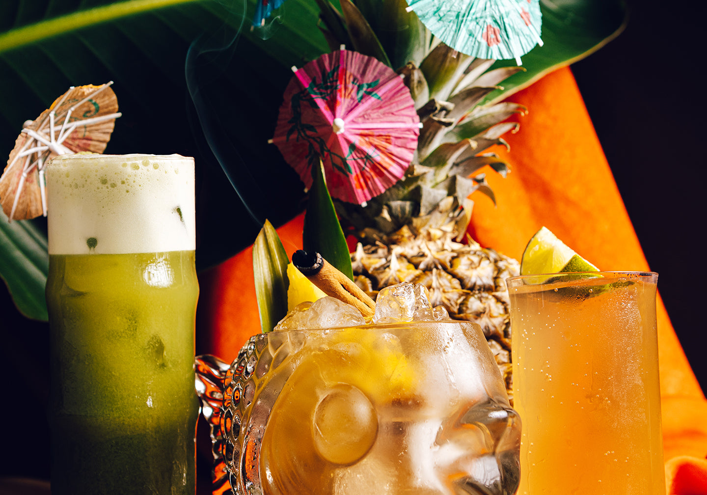 Tropical cocktails with pineapple garnishes and colorful umbrellas on a wooden table.