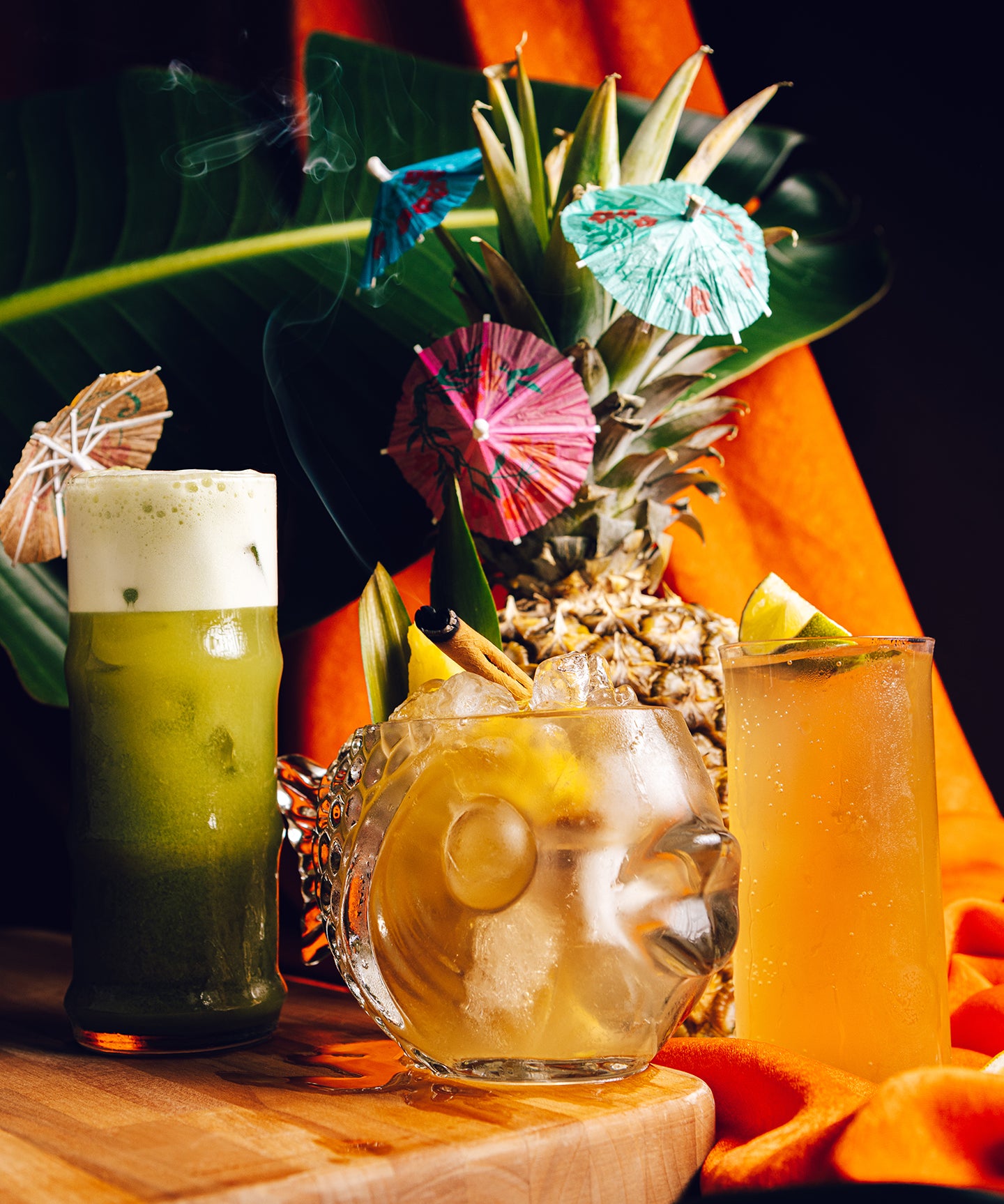 Tropical cocktails with pineapple garnishes and colorful umbrellas on a wooden table.
