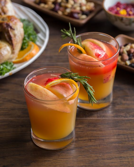 Two glasses of alcohol-free drinks with oranges and rosemary on a table.