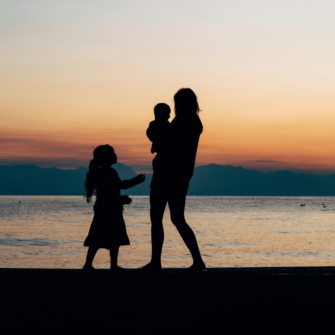 A silhouette of a sober curious mother and child on the beach at sunset.