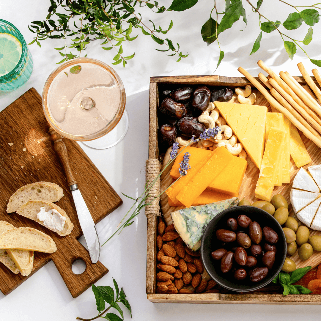 A wooden tray with cheese, crackers, olives and a glass of alcohol-free wine.