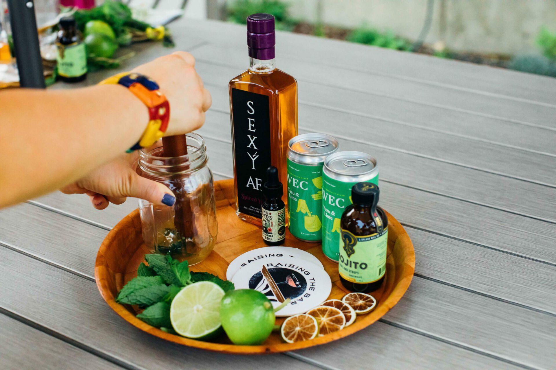 A person preparing a alcohol-free cocktail on a wooden tray for their happy hour subscription box.
