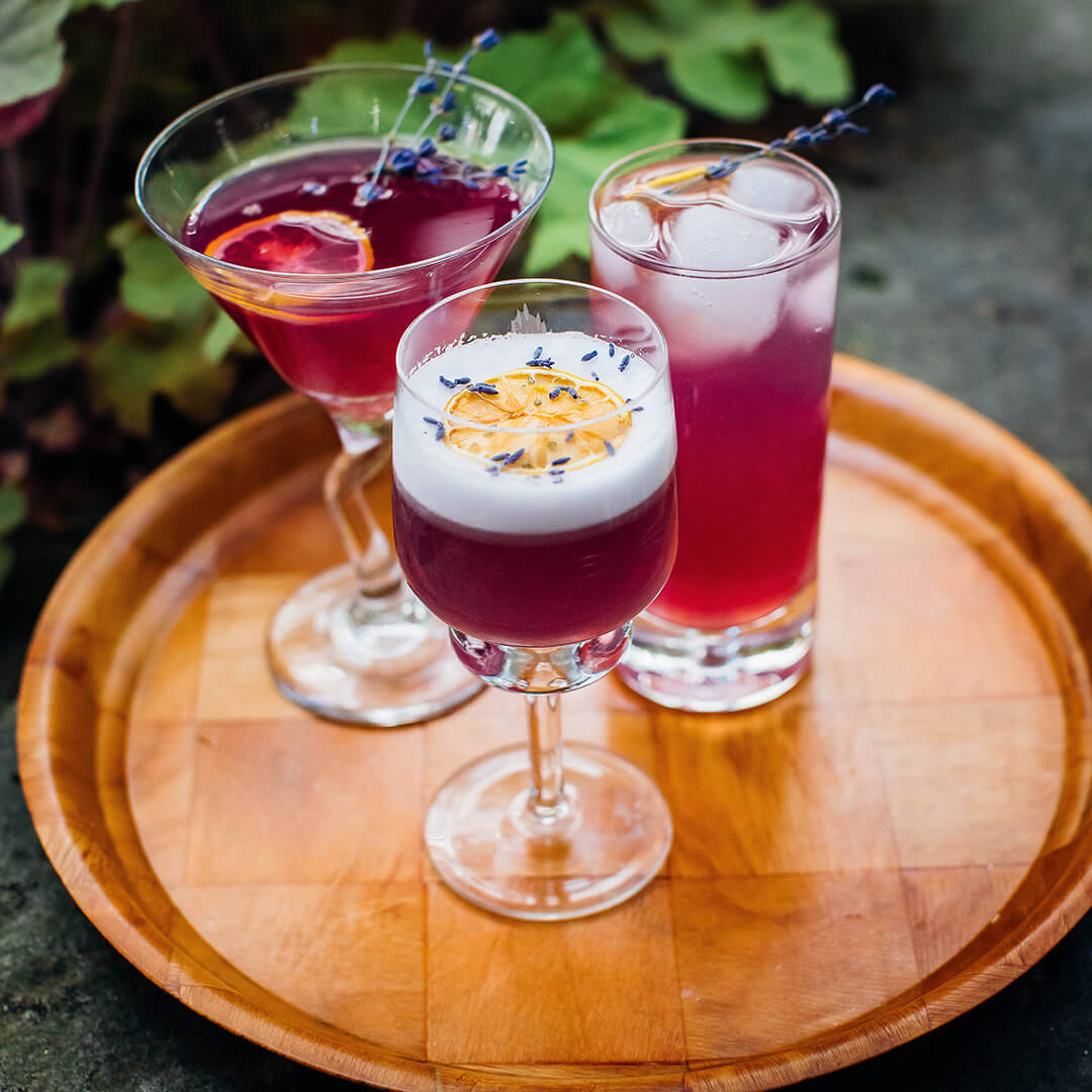 Three zero-proof cocktails on a wooden tray with lavender sprigs.